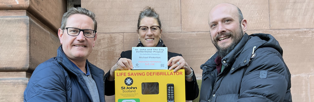 Three people pose with a defibrillator