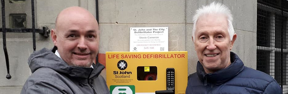 Two men pose with a Public Access Defibrillator
