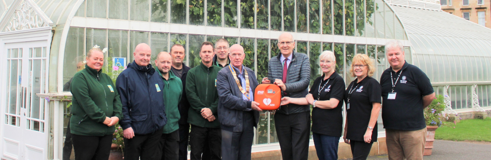 A group of people pose with a defibrillator in front of a glass house